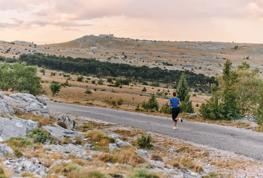 A determined female athlete runs through a forest trail at sunrise, surrounded by breathtaking natural beauty and vibrant greenery.