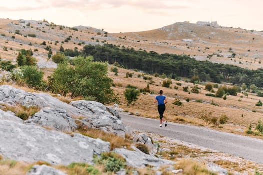 A determined female athlete runs through a forest trail at sunrise, surrounded by breathtaking natural beauty and vibrant greenery.