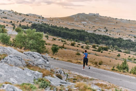 A determined female athlete runs through a forest trail at sunrise, surrounded by breathtaking natural beauty and vibrant greenery.