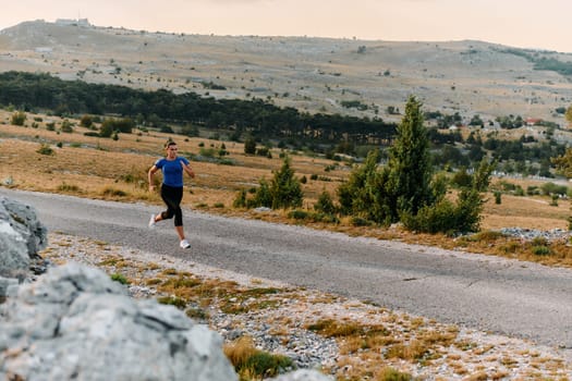 A determined female athlete runs through a forest trail at sunrise, surrounded by breathtaking natural beauty and vibrant greenery.