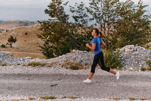 A determined female athlete runs through a forest trail at sunrise, surrounded by breathtaking natural beauty and vibrant greenery.