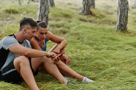 A romantic couple sits in the forest, browsing new running routes on their smartphone, embracing the beauty of nature as they plan their next outdoor adventure together