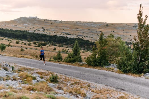 A determined female athlete runs through a forest trail at sunrise, surrounded by breathtaking natural beauty and vibrant greenery.