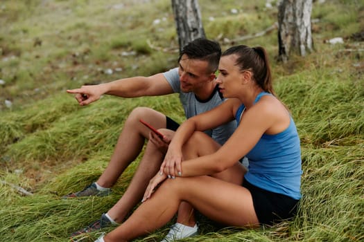 A romantic couple sits in the forest, browsing new running routes on their smartphone, embracing the beauty of nature as they plan their next outdoor adventure together