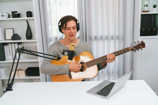Host channel in smart singer with smiling face, playing guitar along singing, broadcasting on social media channel, wearing headphones to record video streamer at modern studio recording. Pecuniary.