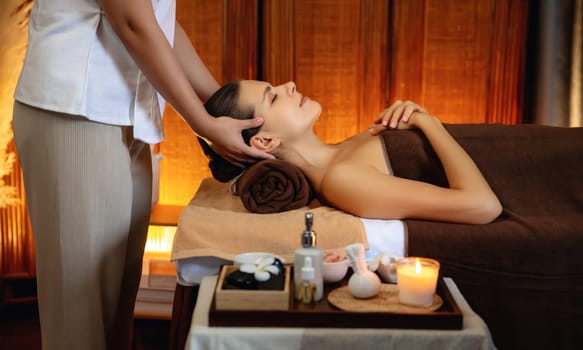 Caucasian woman enjoying relaxing anti-stress head massage and pampering facial beauty skin recreation leisure in warm candle lighting ambient salon spa in luxury resort or hotel. Quiescent