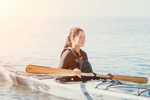 Happy smiling woman in kayak on ocean, paddling with wooden oar. Calm sea water and horizon in background