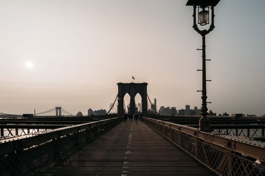 Serene sunrise over Brooklyn Bridge in New York City with skyline in the distance. Tranquil scene capturing early morning light and empty bridge.