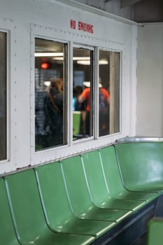 Row of green seats with a no smoking sign on a New York City ferry, reflecting the interior and passengers.