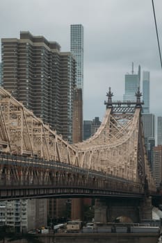 View of the historic Queensboro Bridge with modern skyscrapers in the background under cloudy skies in New York City.