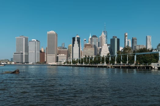 Stunning New York City skyline seen from the waterfront, showcasing skyscrapers and clear blue skies. Vibrant urban landscape on a sunny day.