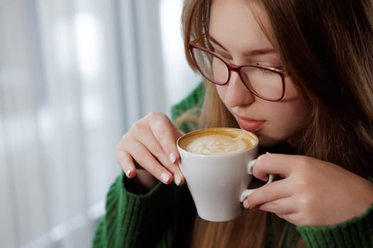 A woman wearing glasses looks happy as she savors a delicious cup of coffee