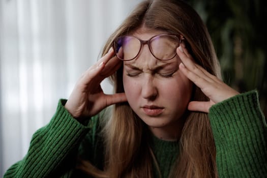 A woman with black hair and wearing glasses appears to be experiencing discomfort as she holds her head with her hand