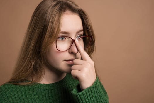 A young woman in a green sweater and glasses is gently touching her nose, showcasing elements like vision care, human body, and eyewear