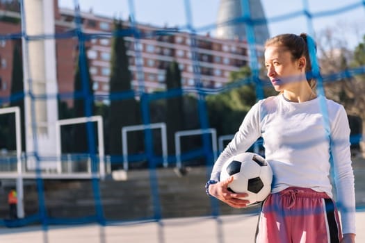 caucasian female football player holding a soccer ball on an urban court, concept of sport and active lifestyle, copy space for text