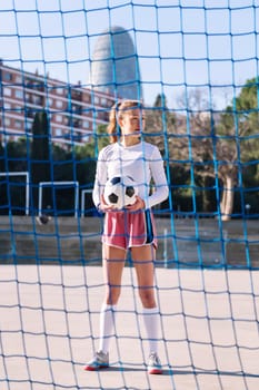 caucasian female football player standing holding a soccer ball on an urban court, concept of sport and active lifestyle