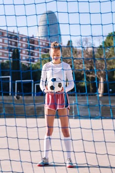 caucasian female football player standing holding a soccer ball on an urban court, concept of sport and active lifestyle