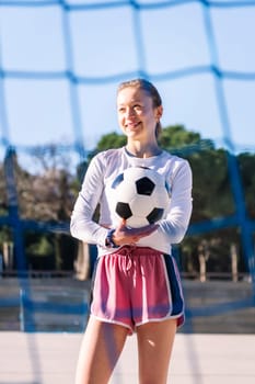 smiling caucasian female football player holding a soccer ball on an urban court, concept of sport and active lifestyle