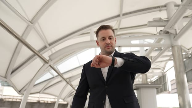 Skilled business man looking watch while walking to train station for going to workplace at bridge. Caucasian manager checking time for important appointment and walk along modern urban city. Urbane.