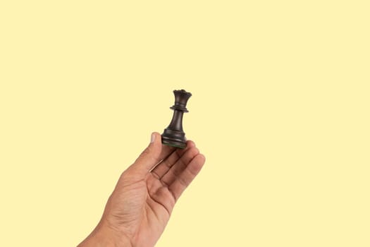 Black male hand holding a black queen chess figure isolated on yellow background. High quality photo