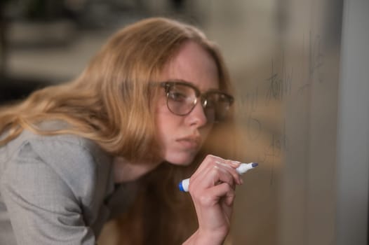 Caucasian woman with glasses writes text in English on a glass wall