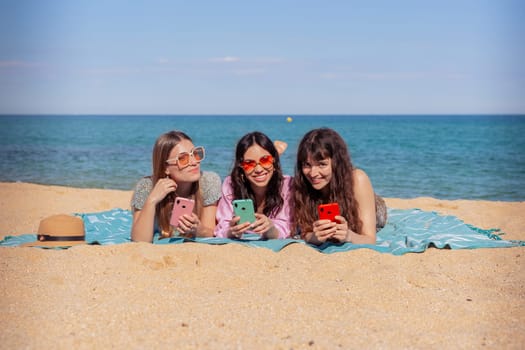 Group of smiling multiethnic women enjoying vacation. Beautiful and cheerful Gen Z girls with their mobile phones pose looking at the camera with a mobile phone.