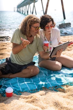 Middle-aged man and woman sitting on the beach with surprised face, browsing tablet apps. Concept:Holidays y Technology