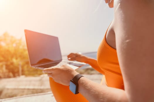 Digital nomad, Business woman working on laptop by the sea. Pretty lady typing on computer by the sea at sunset, makes a business transaction online from a distance. Freelance, remote work on vacation