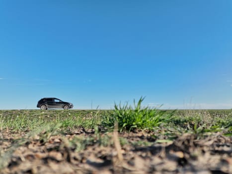 low angle of the green steppe and blue sky with space for text. black car on the side of the road. road trip concept