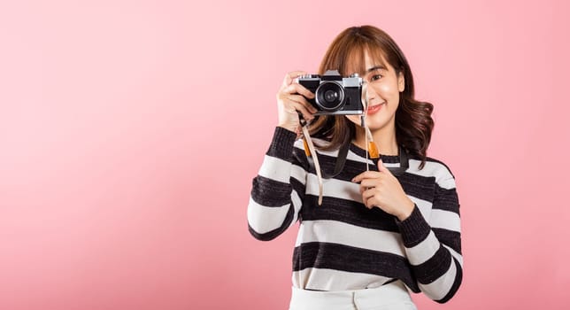 Attractive energetic happy Asian portrait beautiful young woman smiling photographer taking a picture and looking viewfinder on retro vintage photo camera ready to shoot isolated on pink background