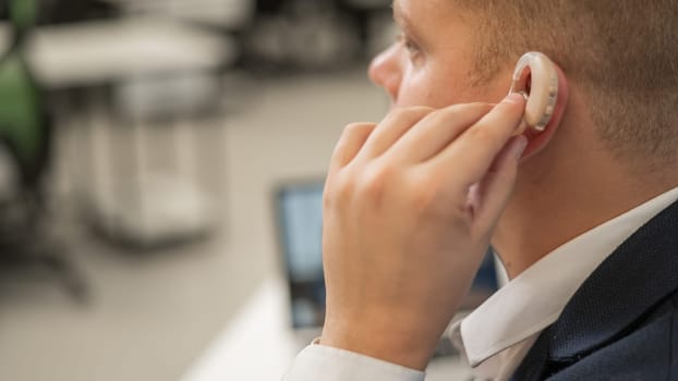 Young caucasian man putting on a hearing aid