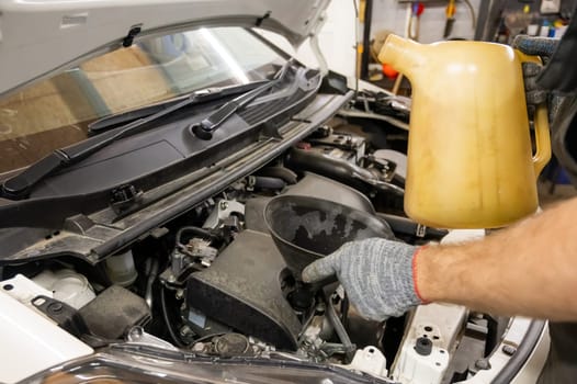 A mechanic fills a car engine with oil. Close-up of a man's hands