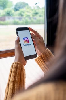 CHIANG MAI, THAILAND - April 30, 2023: A woman holds a smartphone mobile with an Instagram application on the screen is a sharing photo and story videos on the application