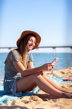 young happy caucasian woman on vacation using smartphone app sitting on towel on the beach