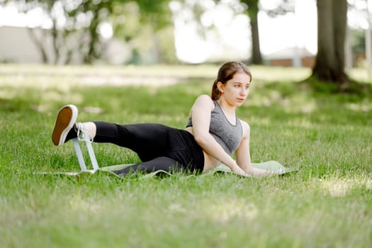 Sporty Girl Exercises With Fitness Band On Grass In Park