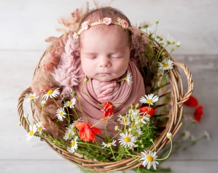 Newborn Baby Girl Sleeps In Basket With Flowers During Studio Photoshoot