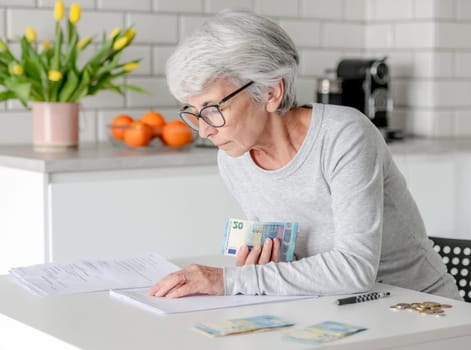 Elderly Woman At Home Holds Euro Money And Examines Documents