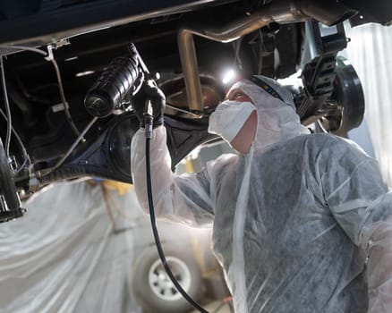 The master sprays an anti-corrosion compound on the bottom of the car