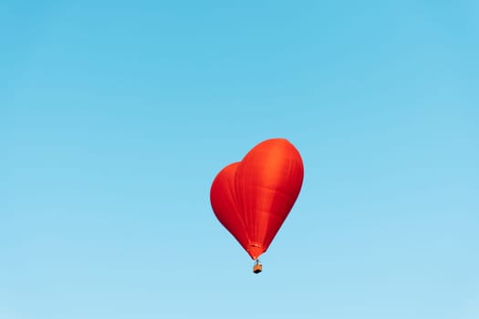 red heart shaped balloon soaring through the clear blue sky on a sunny day