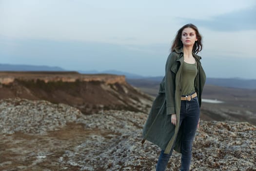 Woman in green coat standing on hill overlooking majestic mountains in the distance