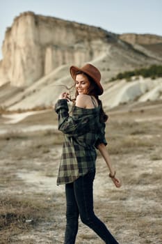 woman in plaid shirt and hat hiking through desert landscape with mountains in background