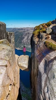 A lone figure stands on the edge of a cliff at Kjeragbolten, Norway, Asian women visit Norway, looking out over the vast expanse below.