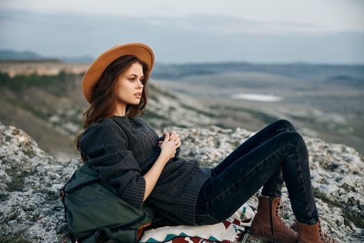 Adventure awaits woman in hat and backpack sits atop mountain, gazing at breathtaking view