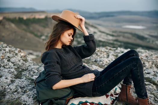 adventure awaits woman with backpack and hat sits on rock, ready for outdoor exploration