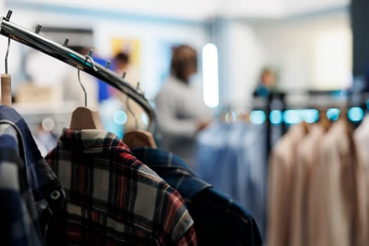 Casual plaid shirts hanging on rack closeup in empty clothing store with blurred background. Stylish outfit on hangers in shopping mall fashion department with no people indoors