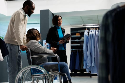 African american woman with chronic impairment getting advice from clothing store assistant while choosing outfit. Mall boutique customer in wheelchair shopping for casual apparel
