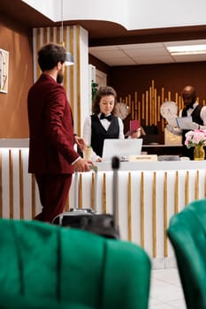 Hotel concierge reviewing id documents to assist businessman with check in process, work trip. Receptionist greeting guest and looking at his passport, online room reservation.