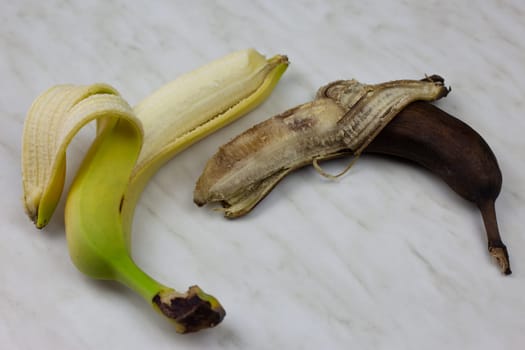 Fresh and spoiled banana on white table, rotten unpleasant fruit lies next to fresh juicy banana, unhealthy fruit food