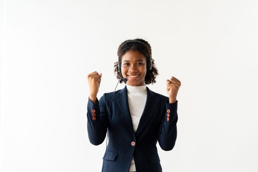 Confident female call center employee wearing a headset and business attire, celebrating success with a smile in a modern office environment.