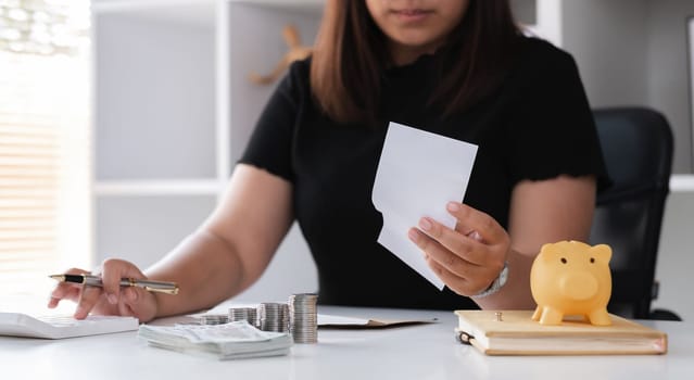 Young woman planning to save money by budgeting and organizing finances at home, using a calculator, counting coins, and managing bills.